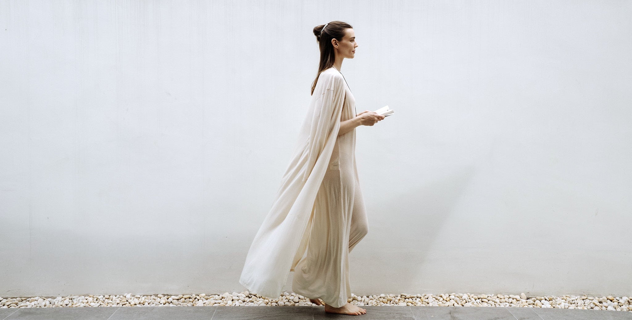 Woman in a white dress standing against a white wall with a minimal background