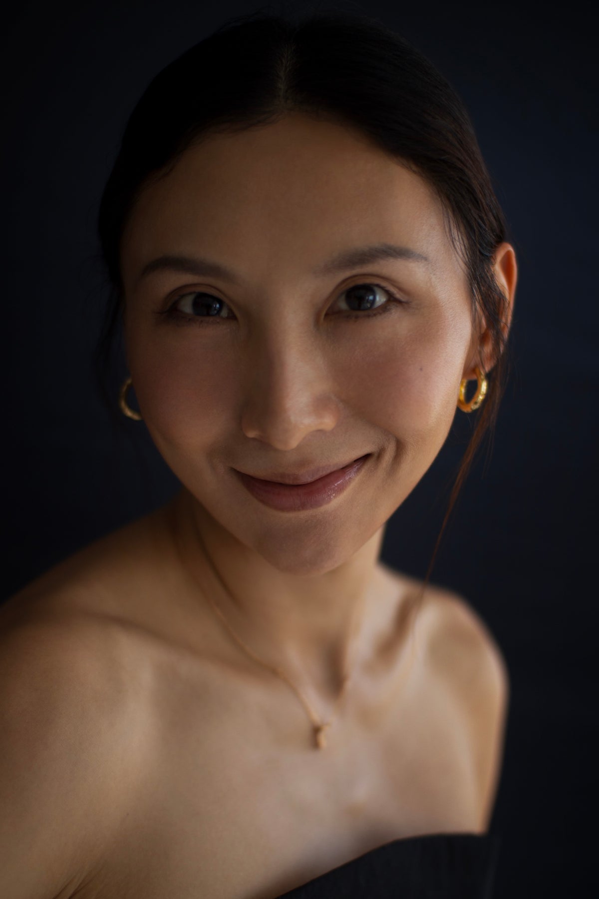 A woman smiling softly against a dark background.
