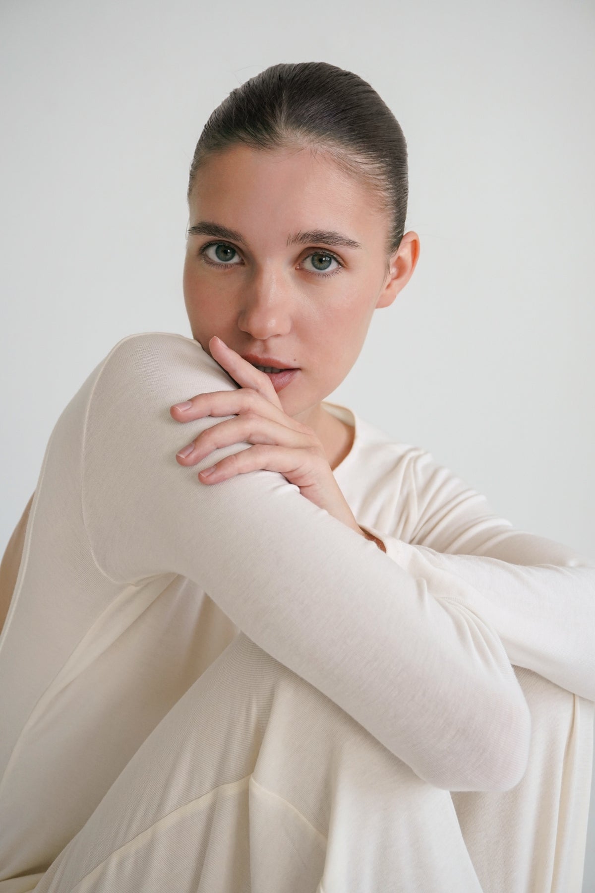 A woman resting her hands near her face in a light outfit.